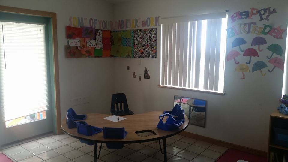 Classroom with a round table and chairs, bulletin board, and window blinds