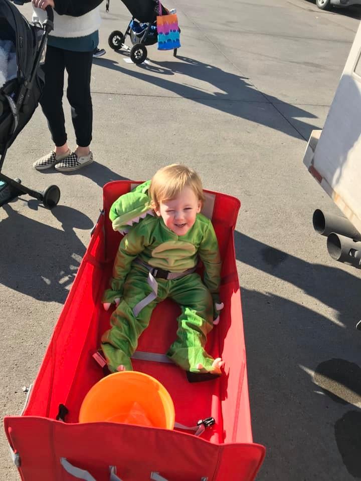 Child in a green costume sitting in a red wagon