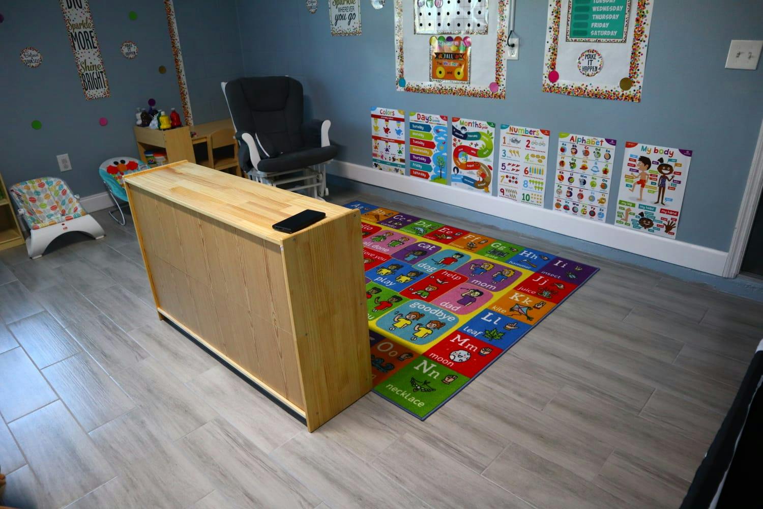 A wooden cabinet in a room with a colorful alphabet rug