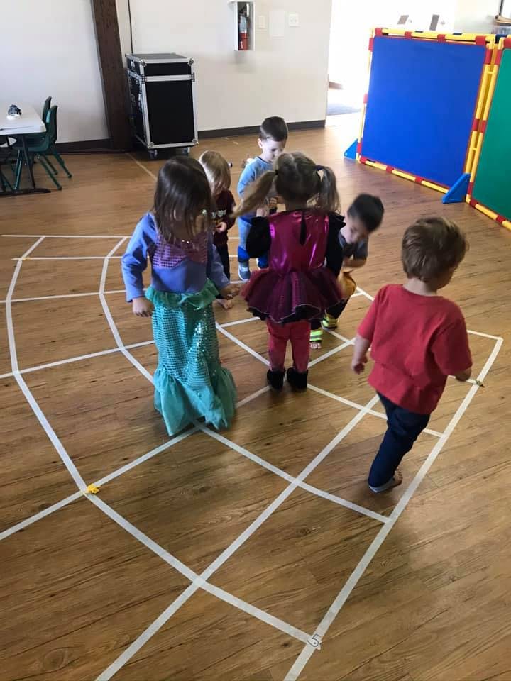 Children playing on a grid of tape on a wooden floor