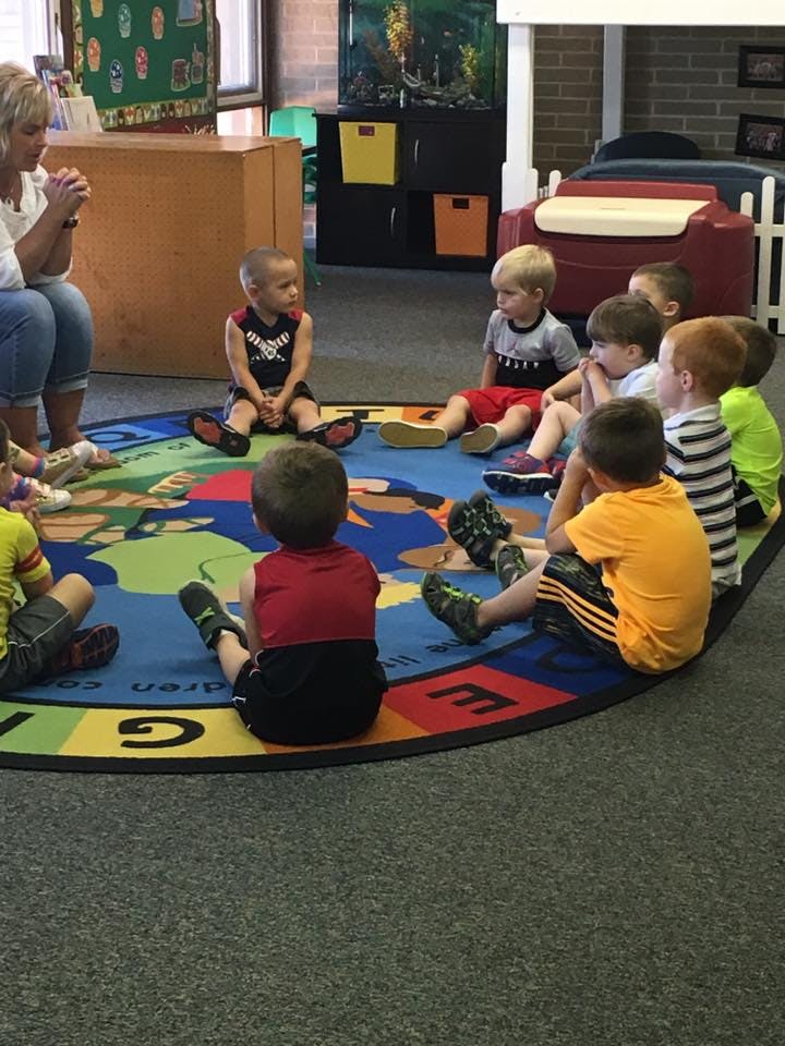 Adult and children sitting on a colorful rug in a classroom
