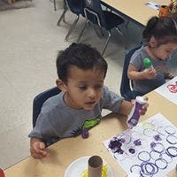 Child painting with a bottle of paint at a table