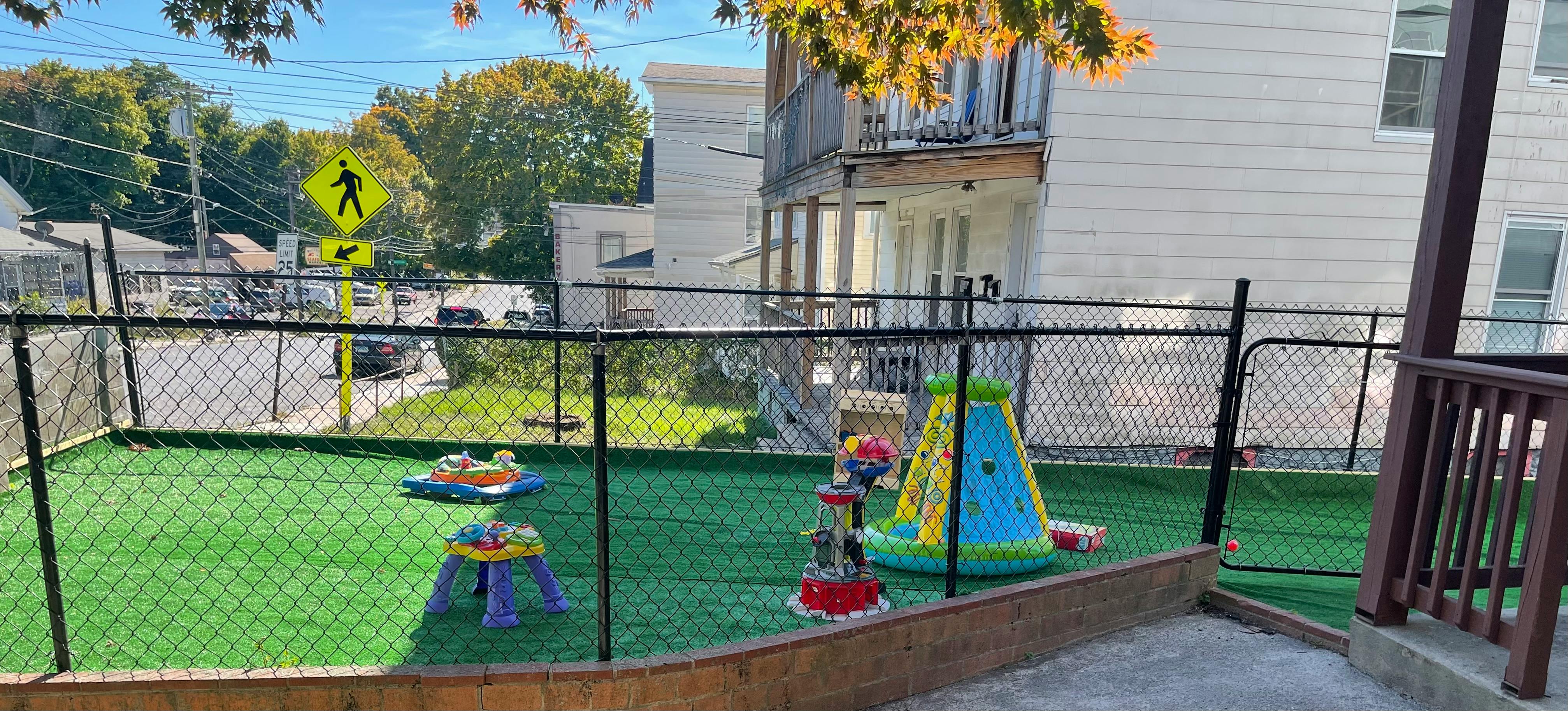 Fenced outdoor play area with artificial turf and colorful play equipment