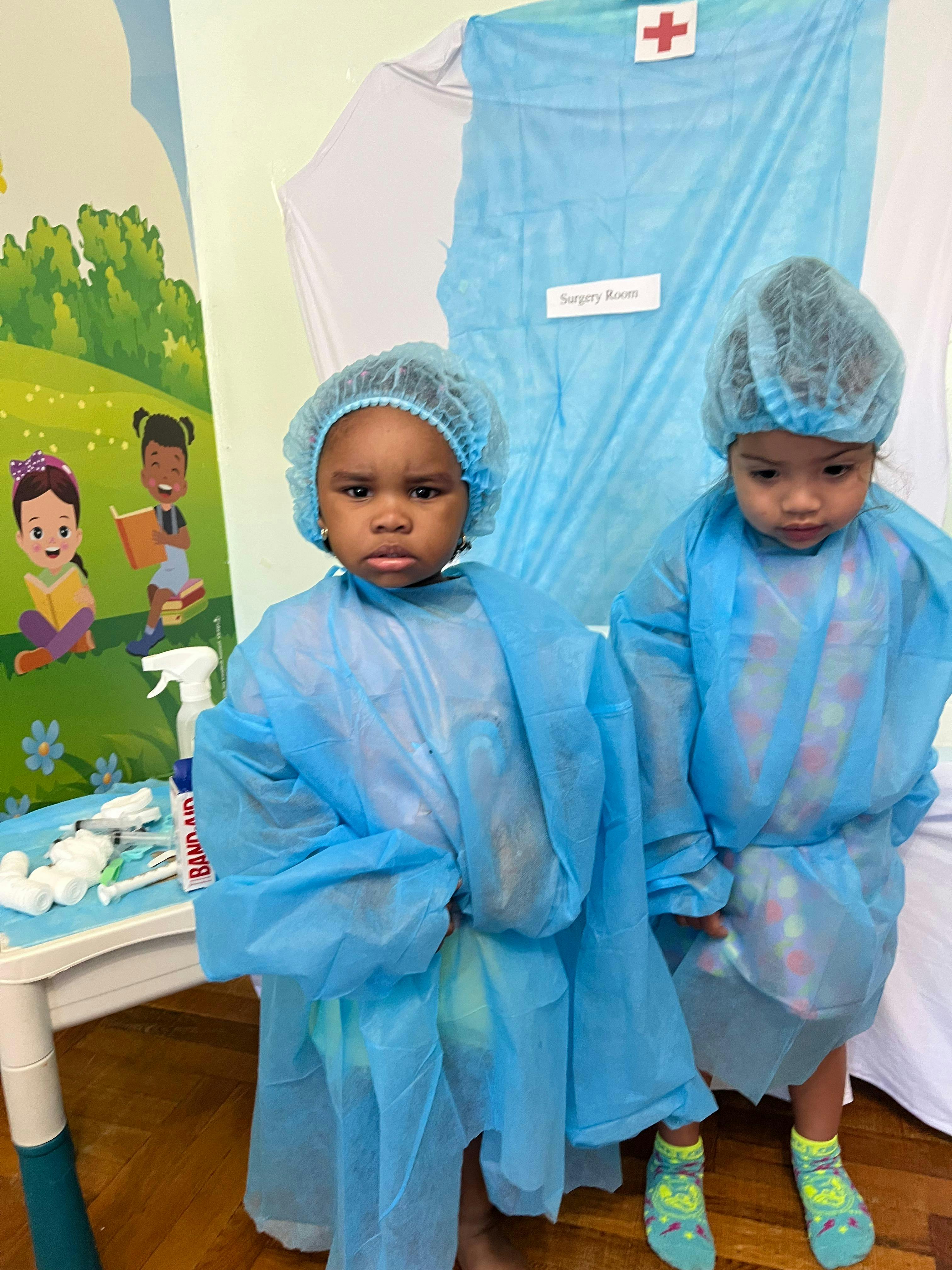 Two children wearing medical caps and gowns in a play surgery room
