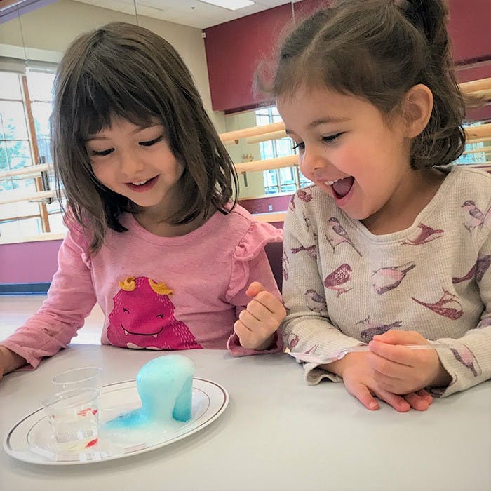 Two children watching a science experiment with blue foam