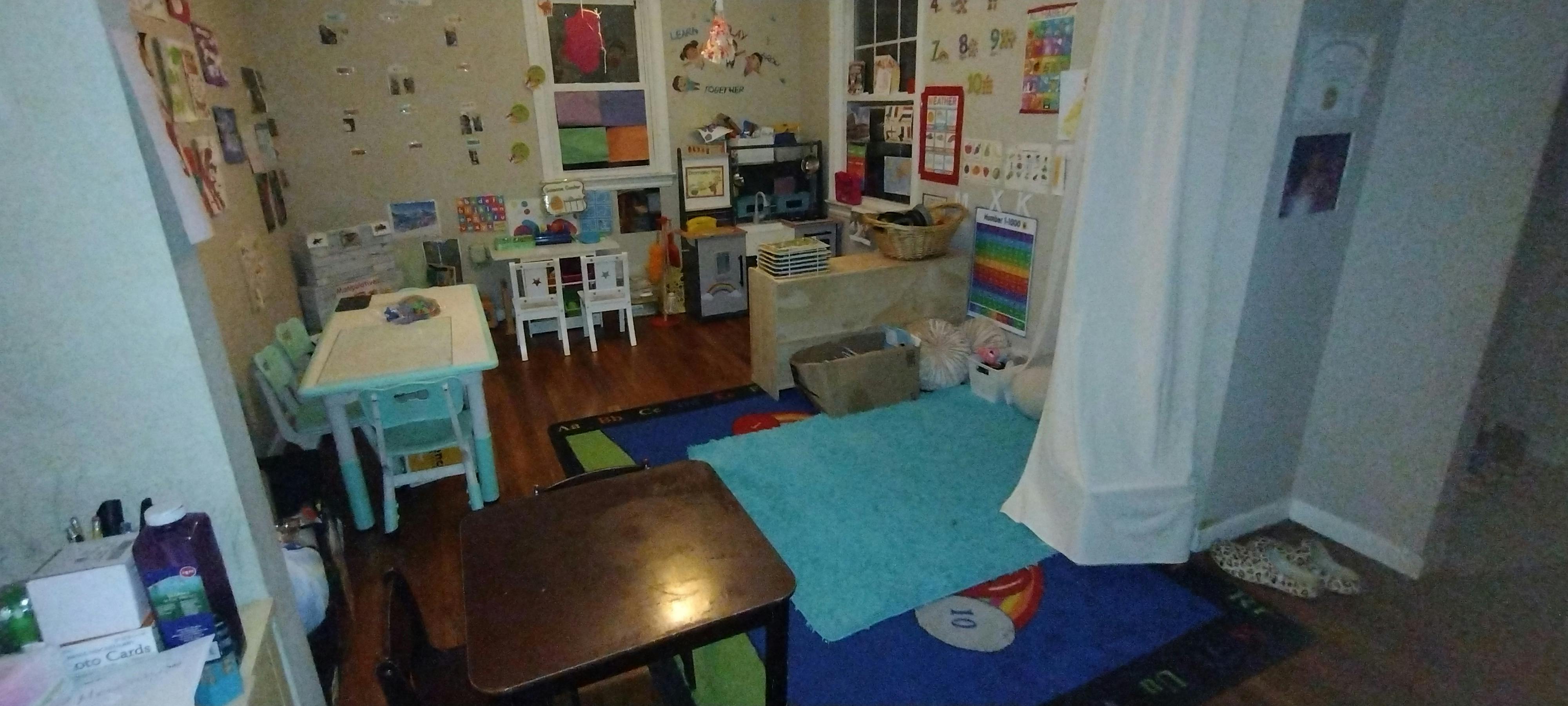 A playroom with two small tables, two small chairs, a teepee, and educational posters