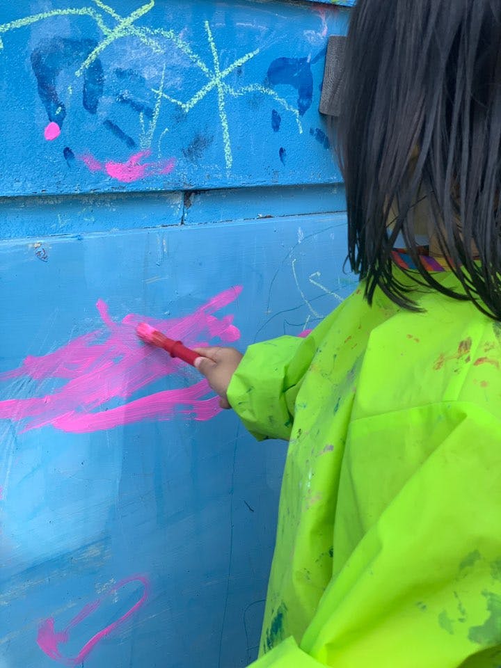 Child in a neon smock painting on a blue surface