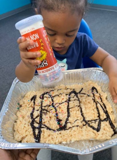 Child sprinkling colorful candy onto a dessert in a foil pan