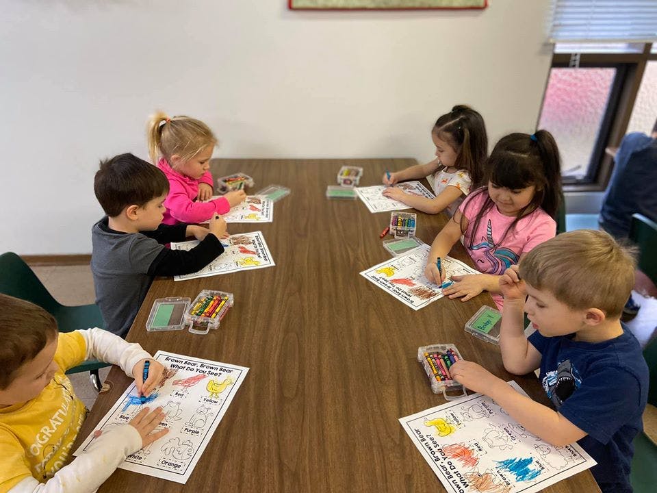 Children sitting at a table coloring on papers