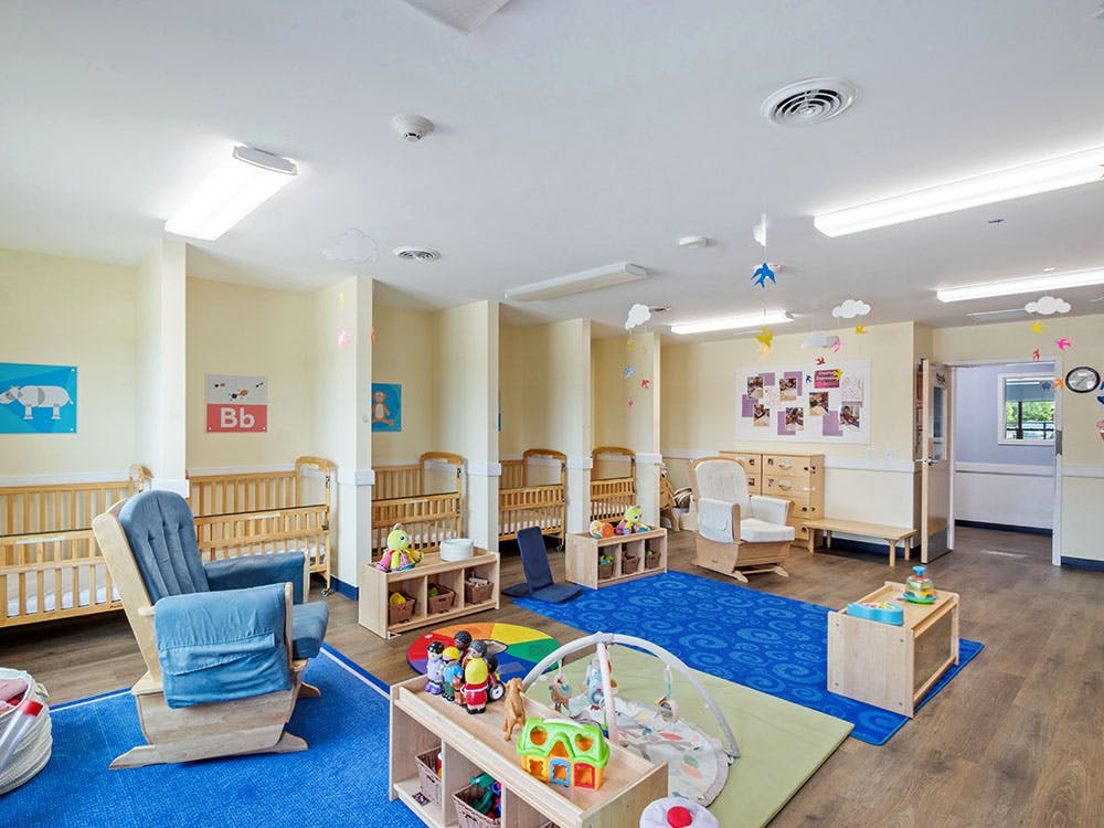A colorful daycare room with several cribs, rocking chairs, and toys