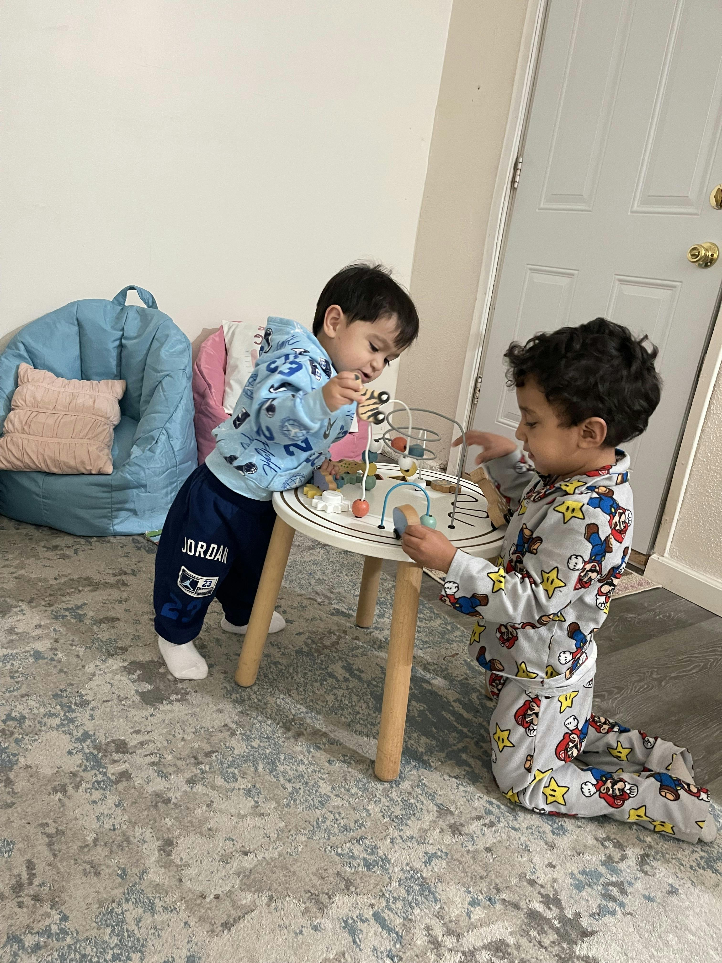 Two young children playing with a bead maze on a small table