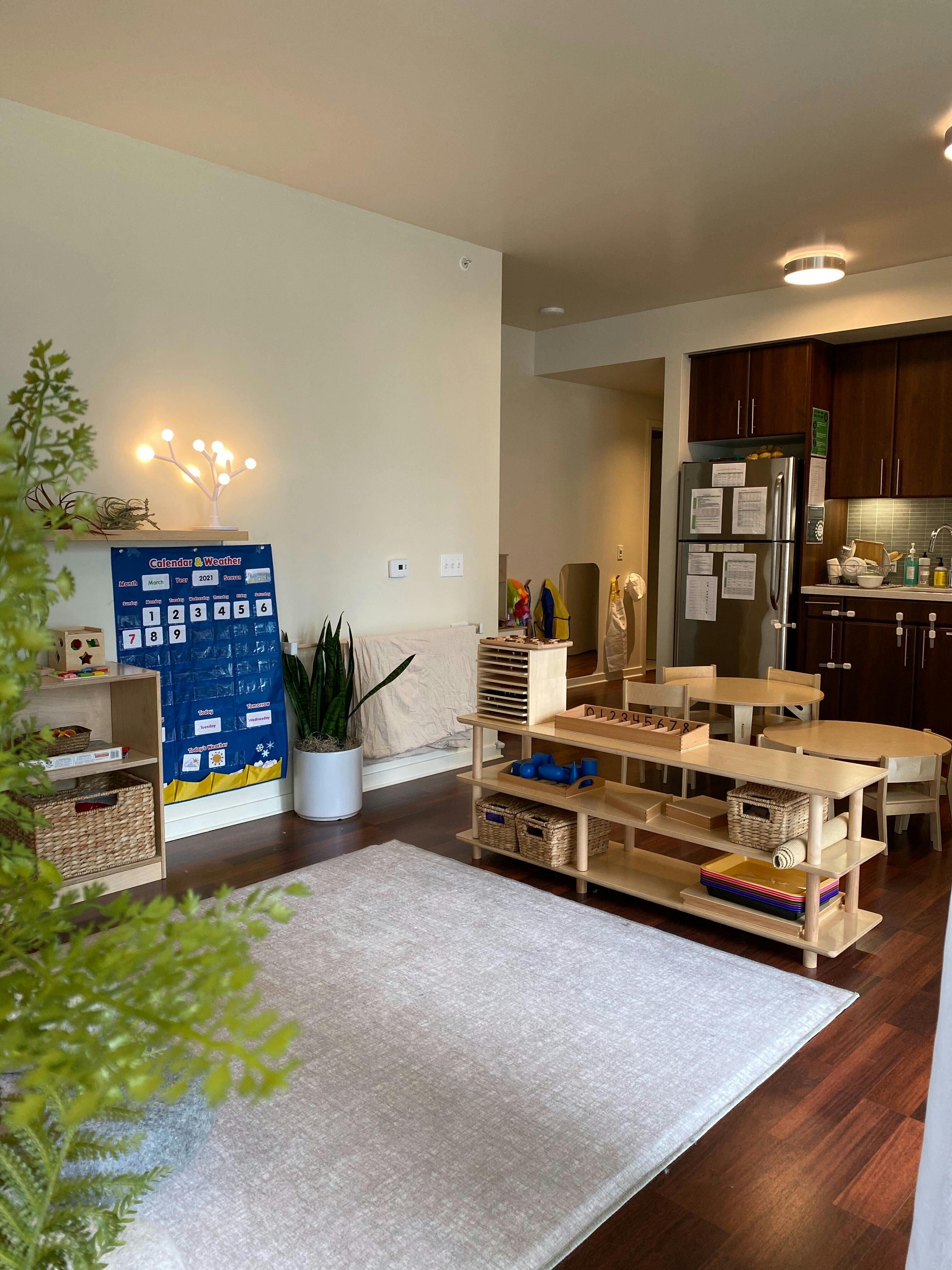 Montessori classroom with wooden shelves, tables, and a blue calendar chart