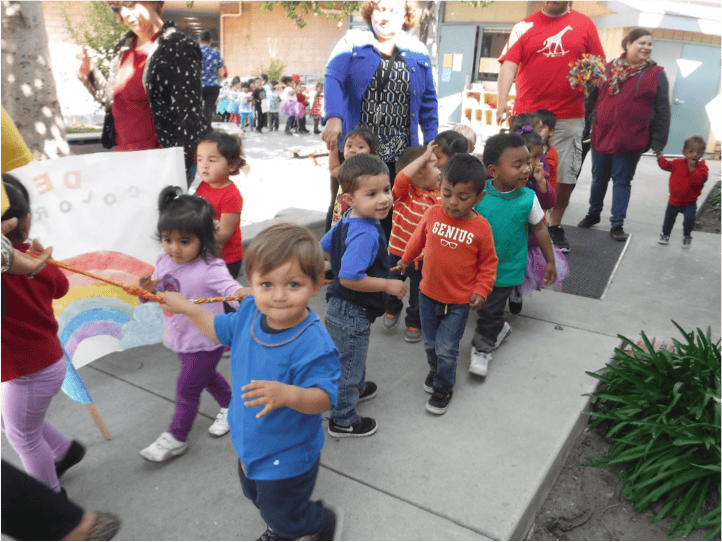 Children walking outdoors, one holding a rainbow flag