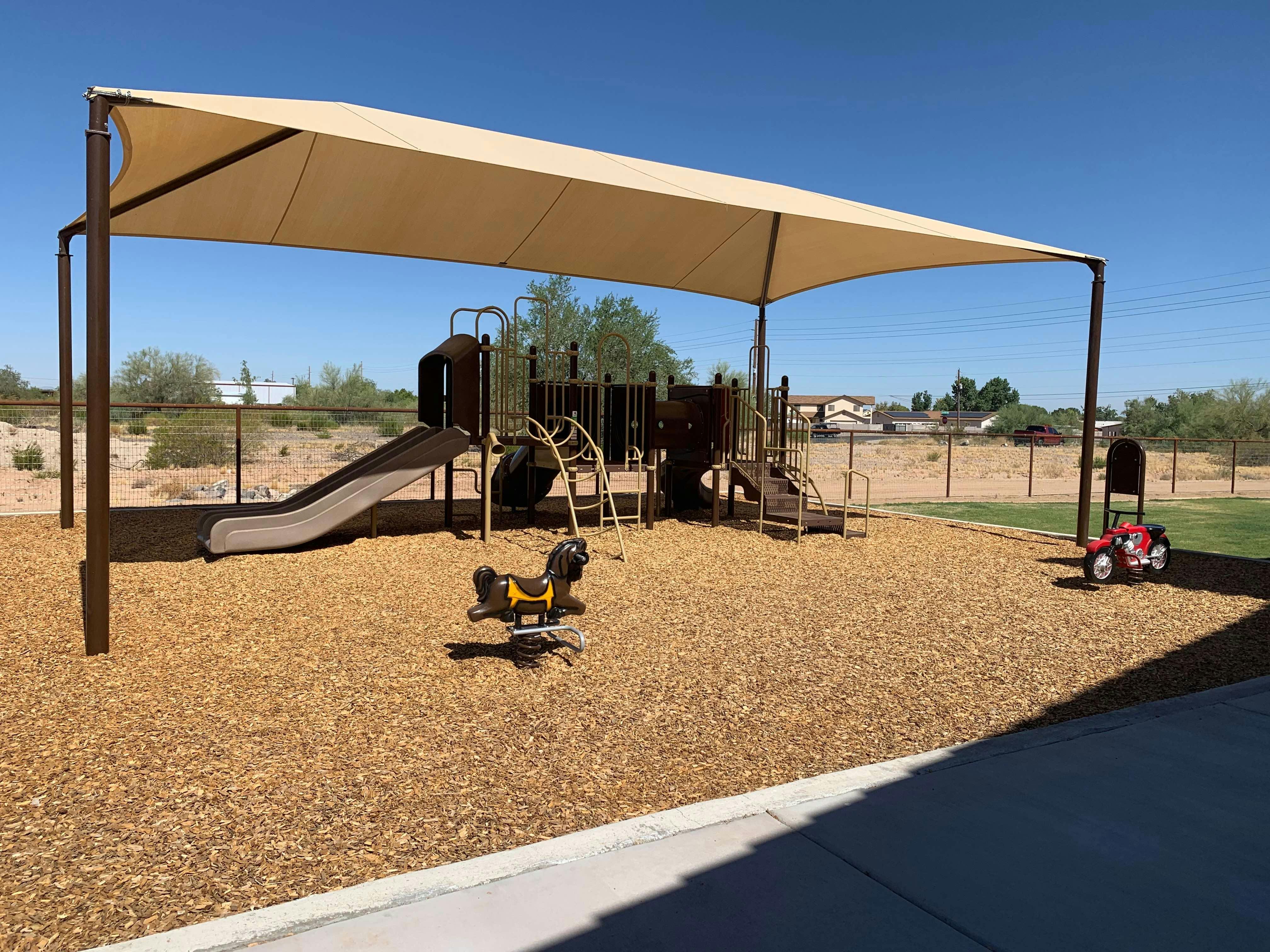 Playground with a slide, climbing structure, and spring rider under a shade canopy