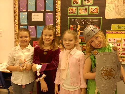 Four children posing in a classroom, one in a knight costume