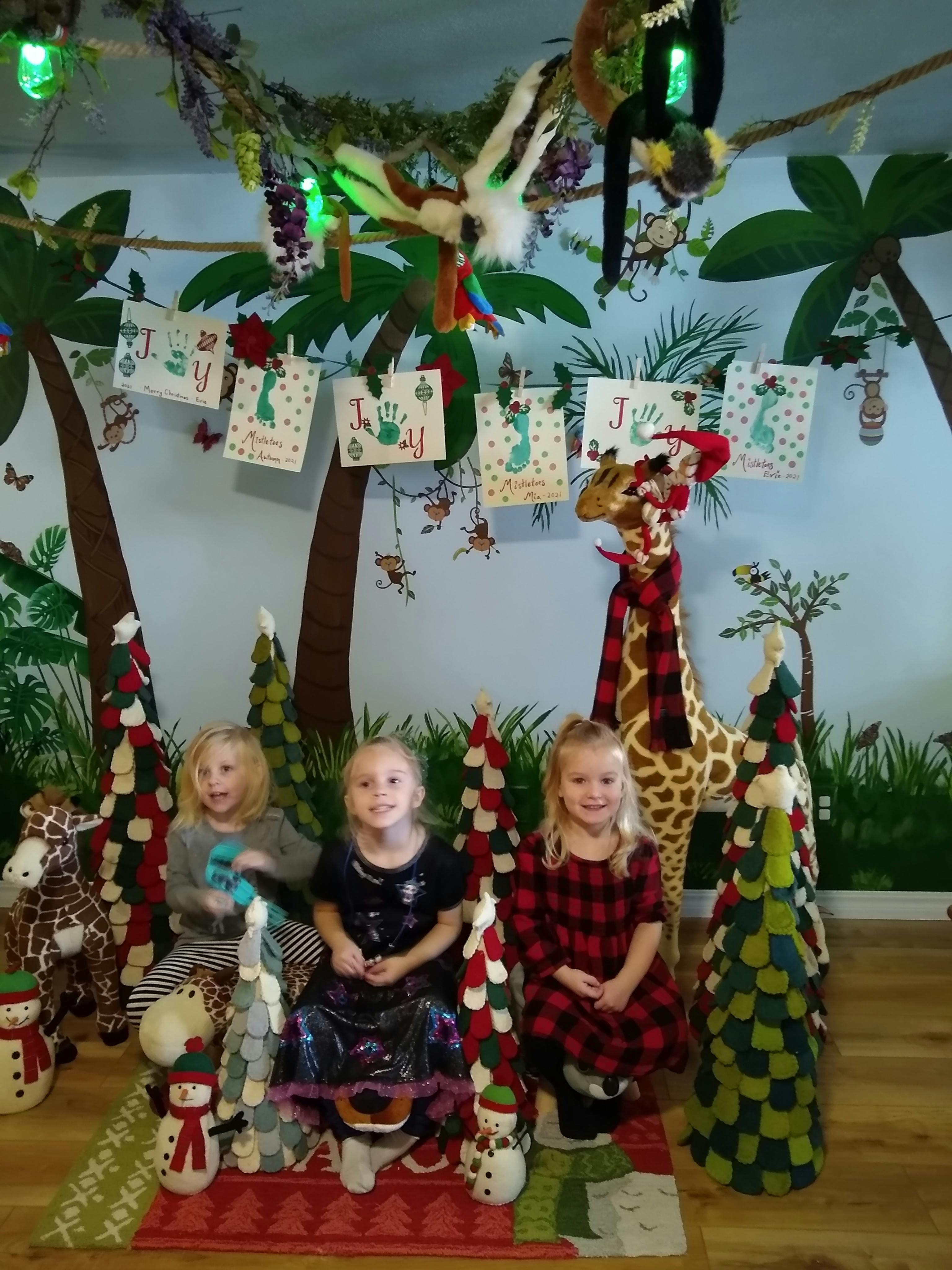 Three children sitting with Christmas decorations and a giraffe statue