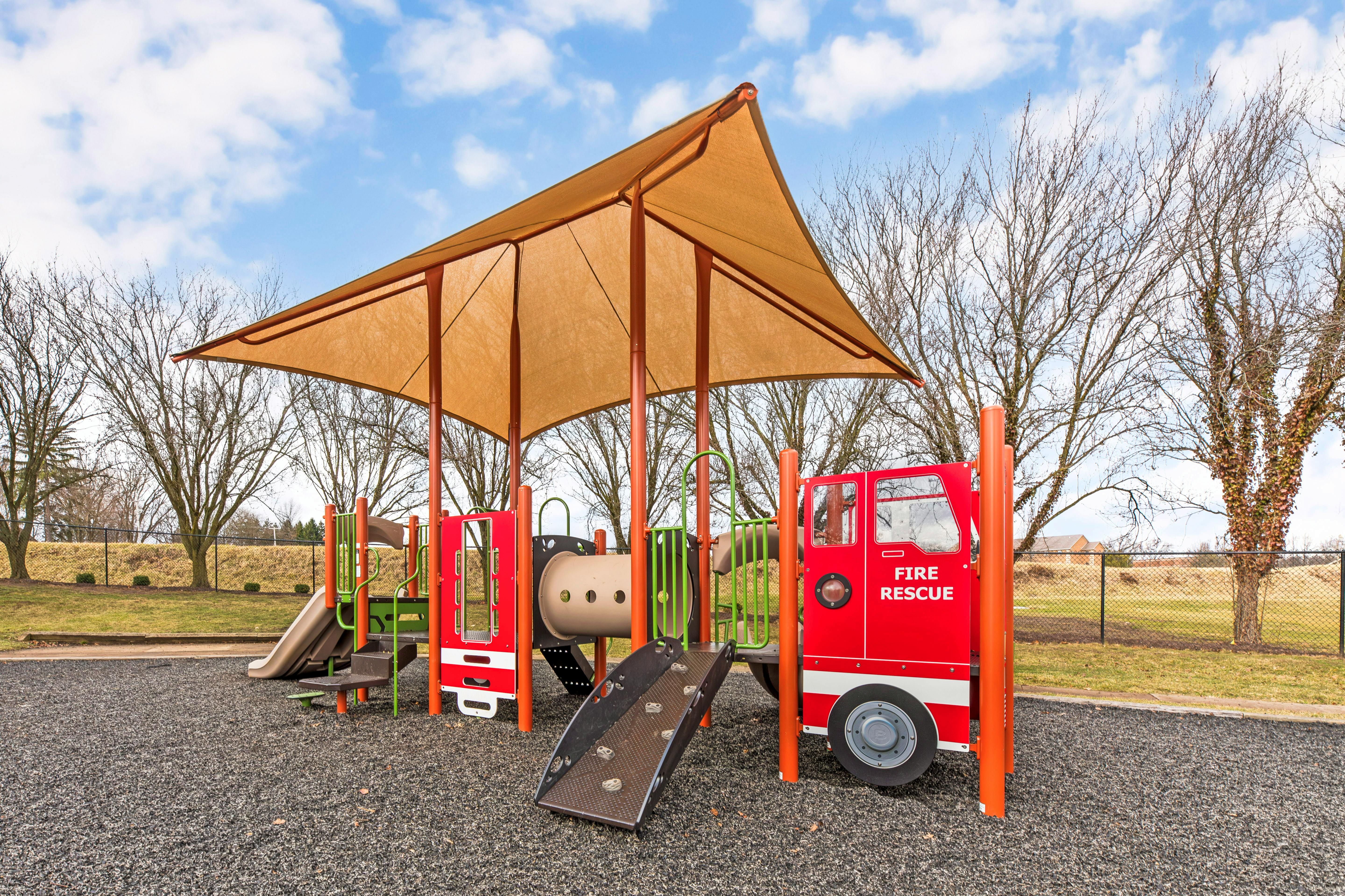 Playground with fire rescue truck facade, climbing wall, tunnel, and slides
