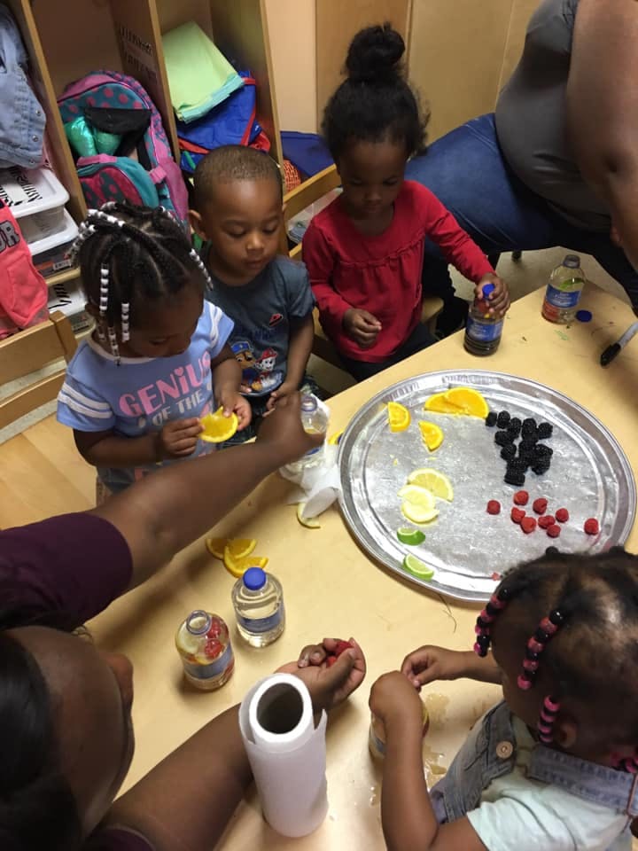 Children and an adult preparing fruit and drinks at a table