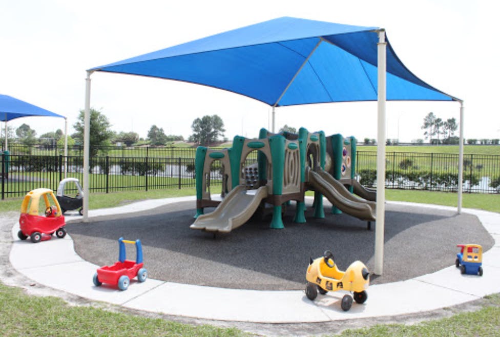 Playground with slides and small ride-on toys under a blue shade canopy