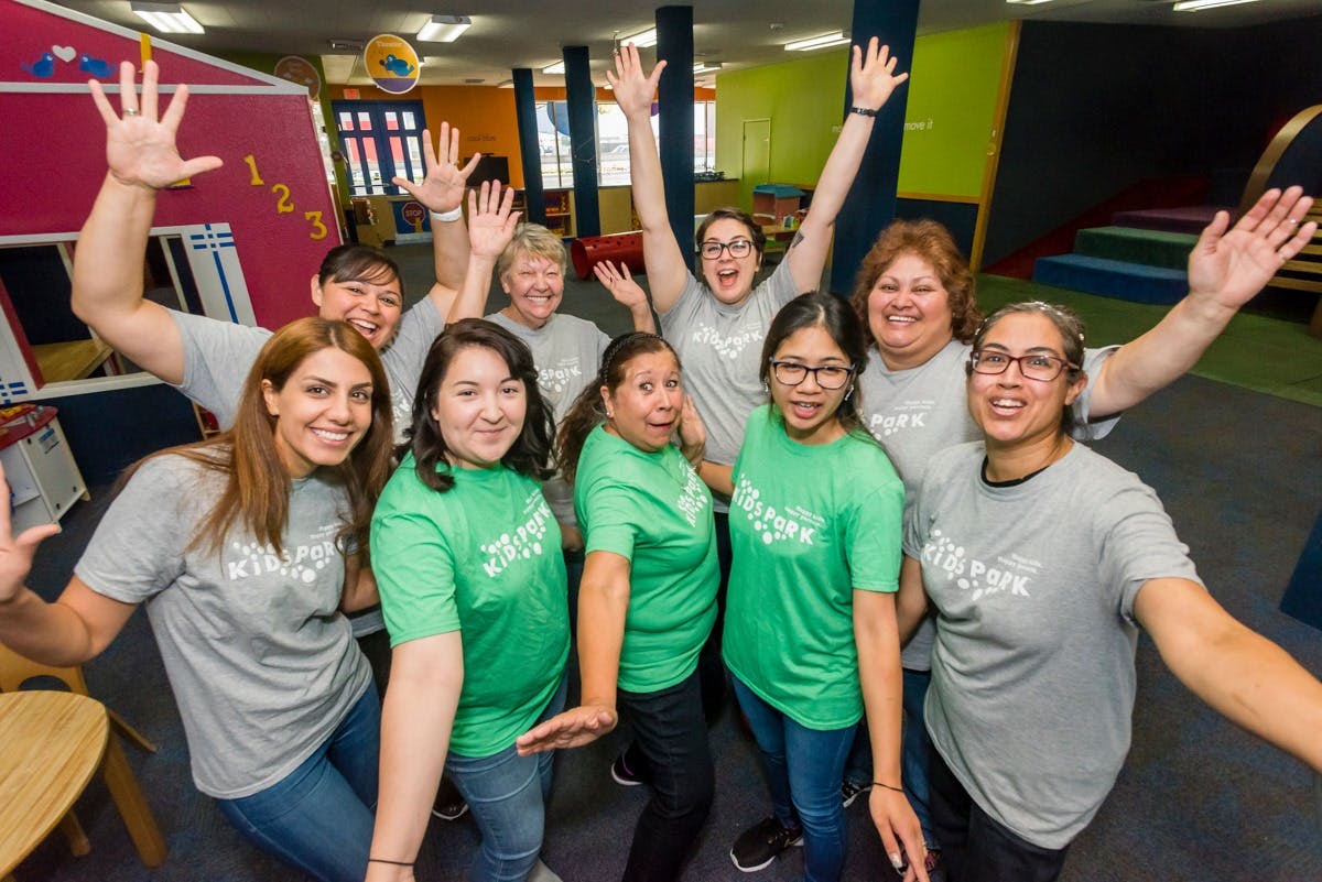 Group of people in green and gray shirts with arms raised