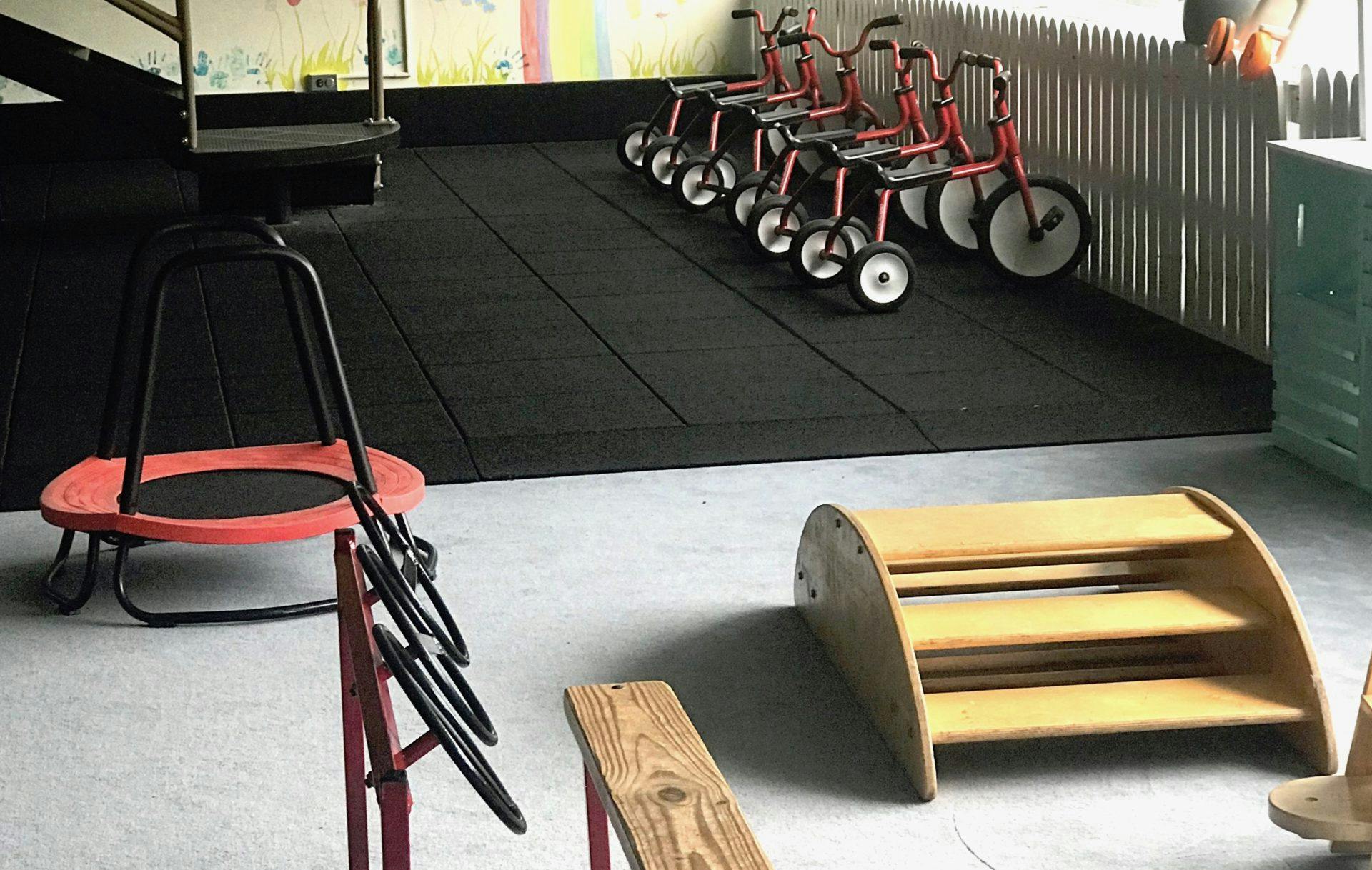Children's play area with small tricycles, a trampoline, and wooden play equipment