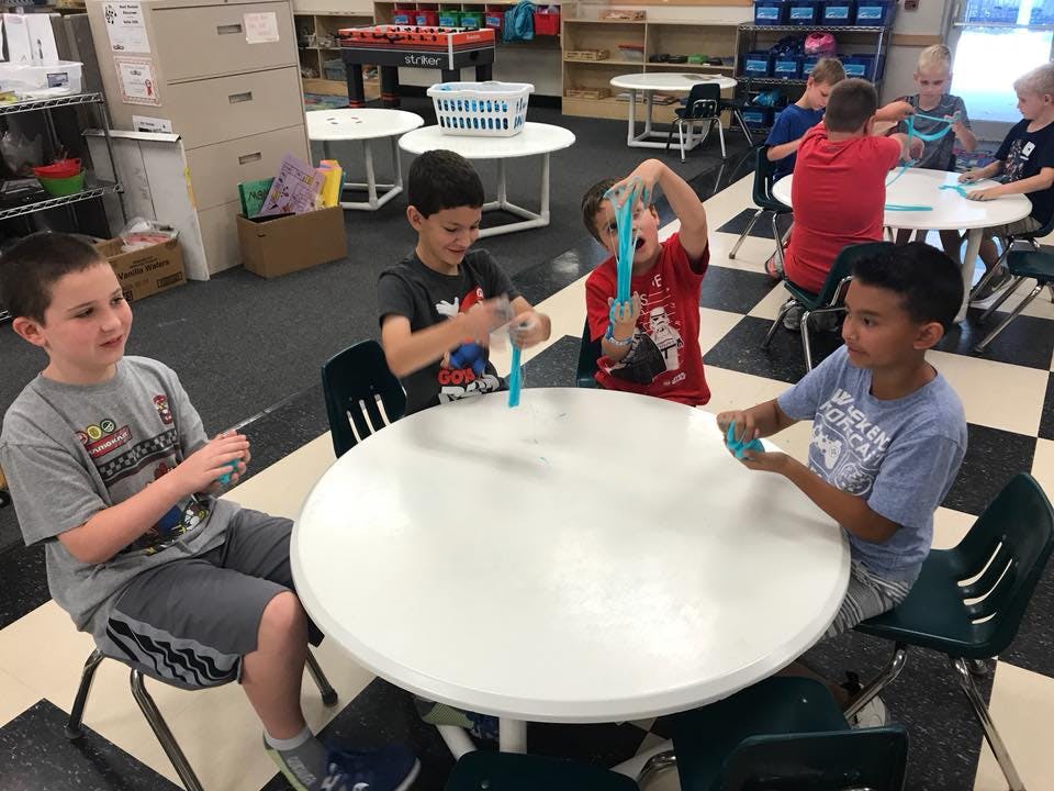 Children playing with slime at a table in a classroom