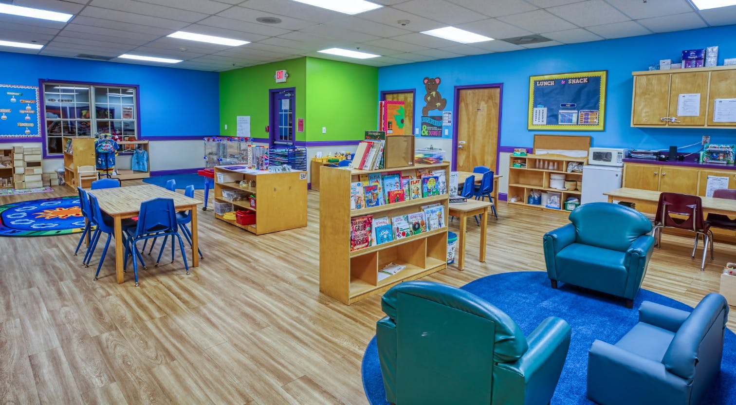 Colorful classroom with tables, chairs, a bookshelf, and a blue rug