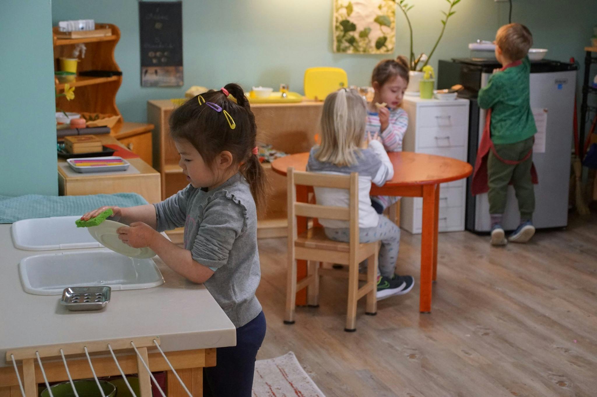 Child washing dishes in a classroom with other children