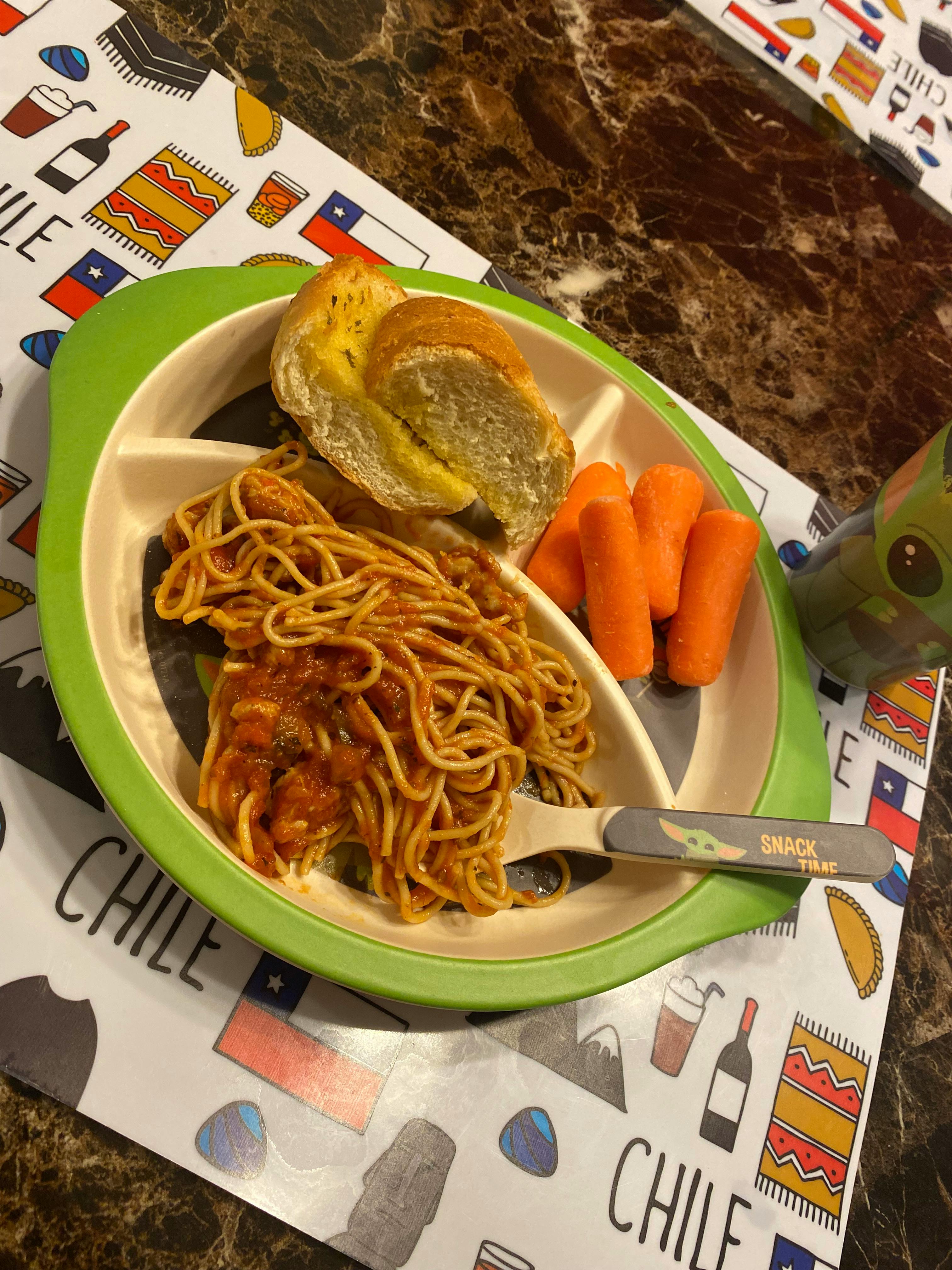 Spaghetti with sauce, garlic bread, and carrots on a divided plate