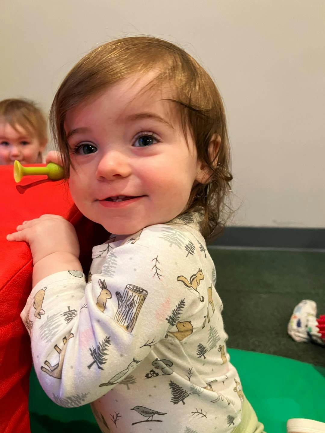 Child smiling, holding onto a red object