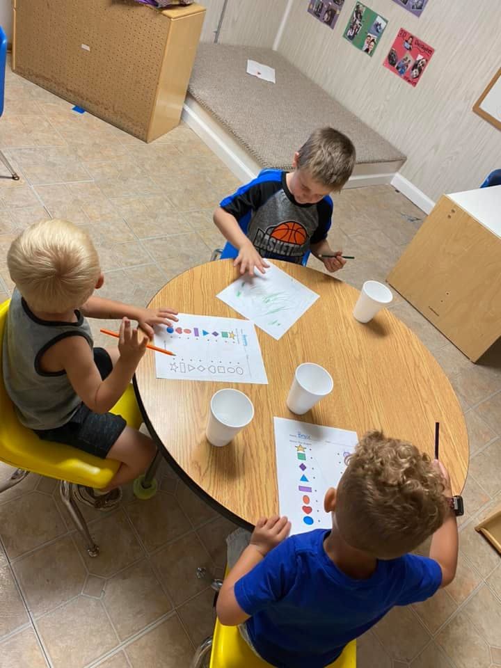 Three children drawing at a round table in a classroom