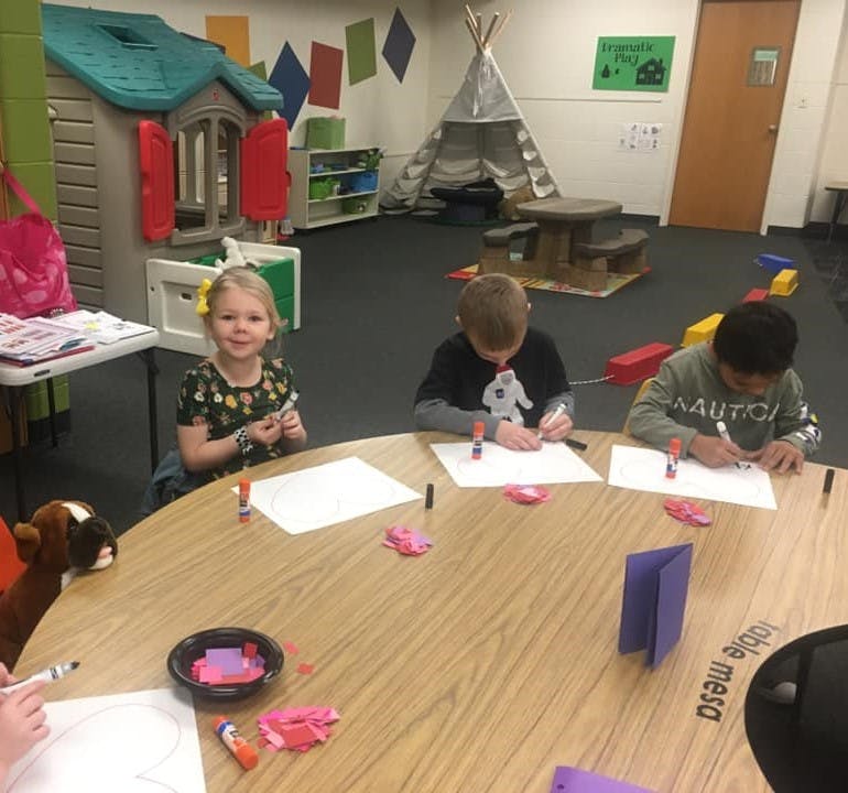 Three children drawing at a table in a classroom