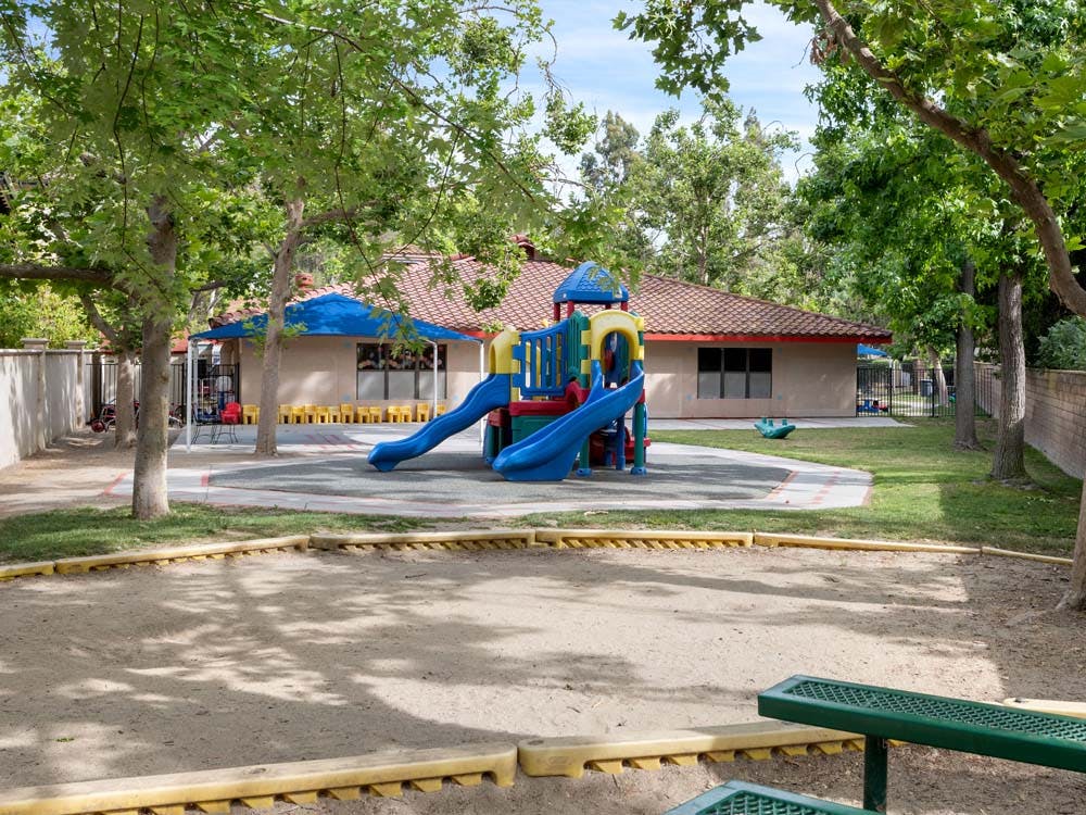 Playground with a colorful playset, sandy area, and a building in the background