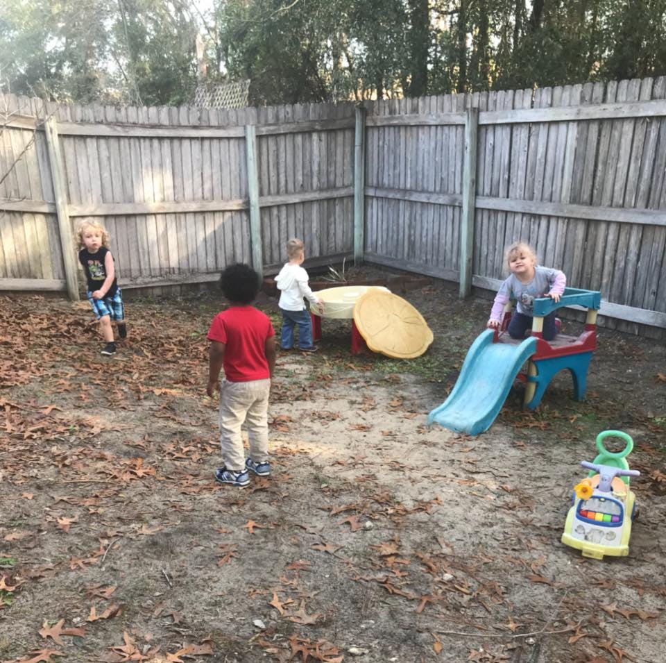 Children playing in a fenced yard with a slide and sand table