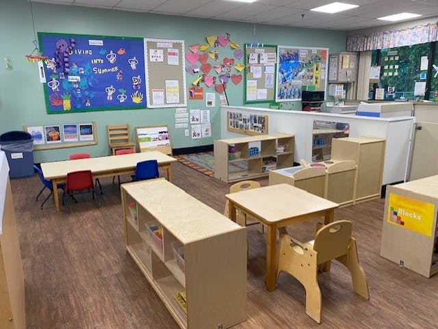 An empty classroom with bulletin boards, small tables, chairs, and shelves