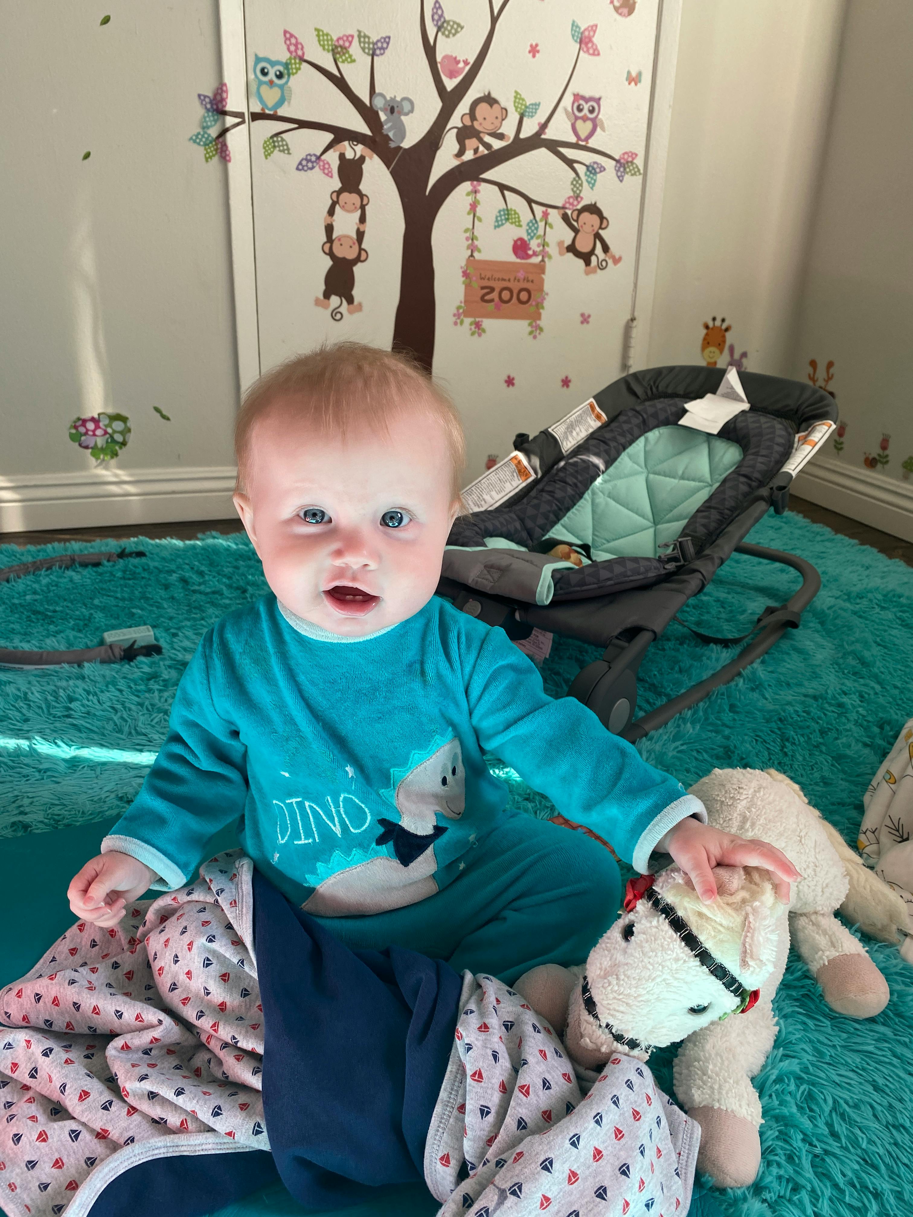 Child in blue pajamas with a dinosaur graphic sitting on a rug next to a toy
