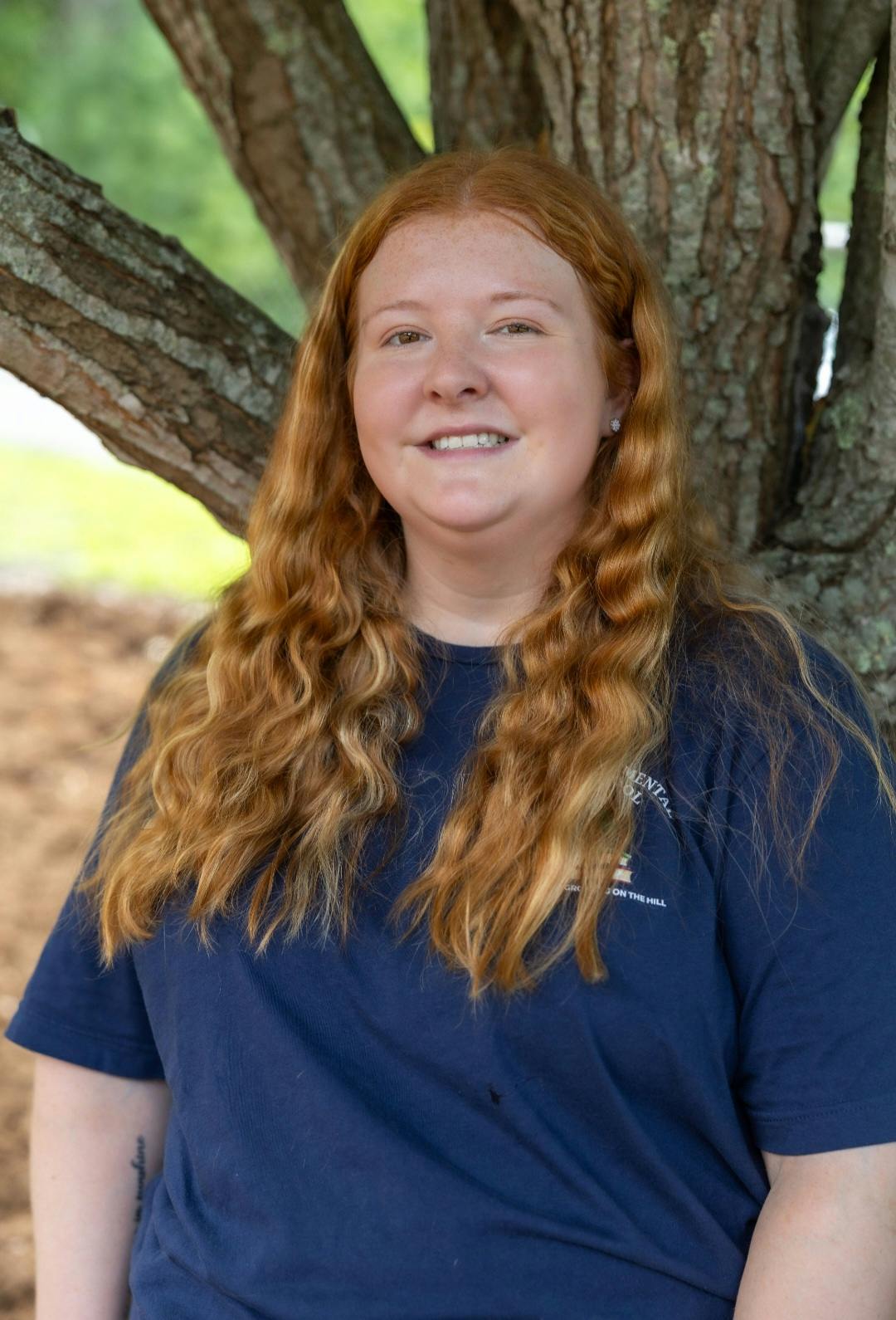 Person with long red hair standing in front of a tree