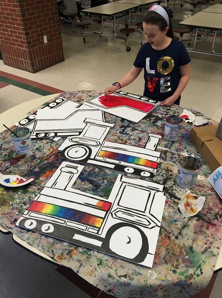 Child painting a truck cutout red at a table