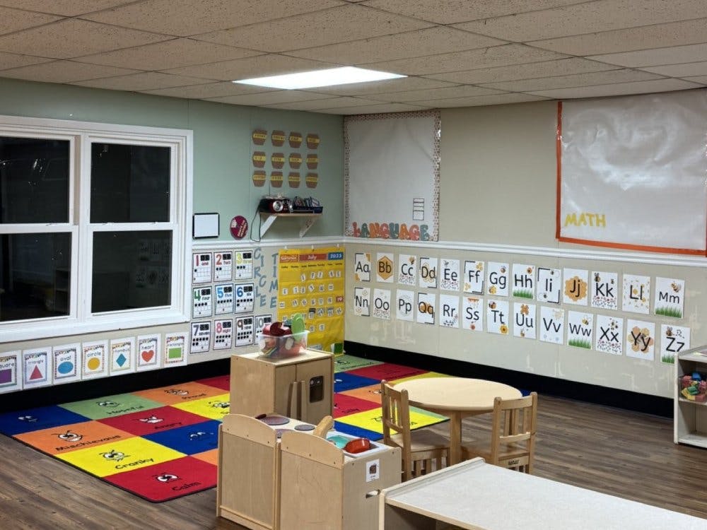 Classroom with colorful rug, small tables, and alphabet/number charts on walls