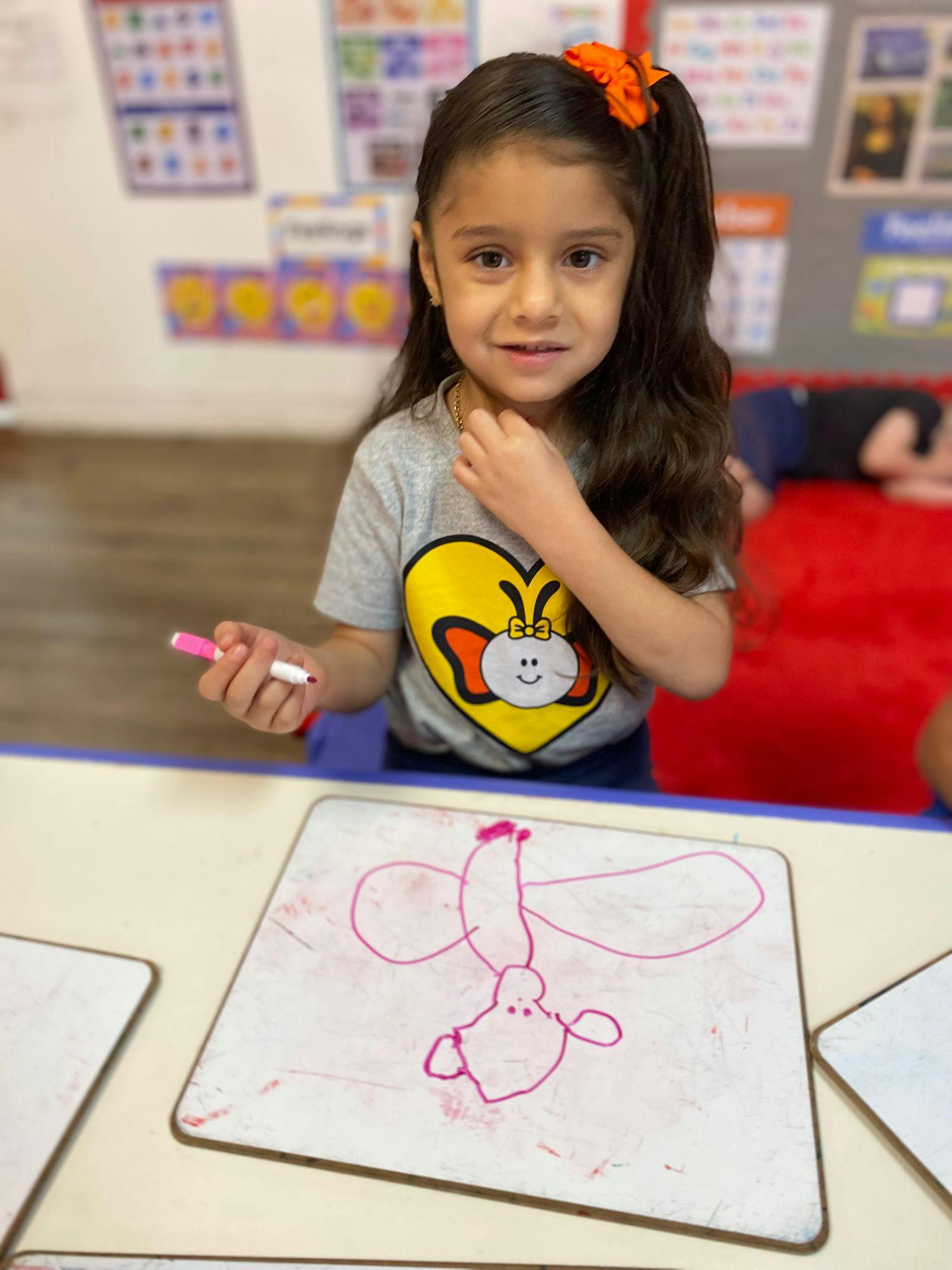 Child drawing on a whiteboard with a pink marker