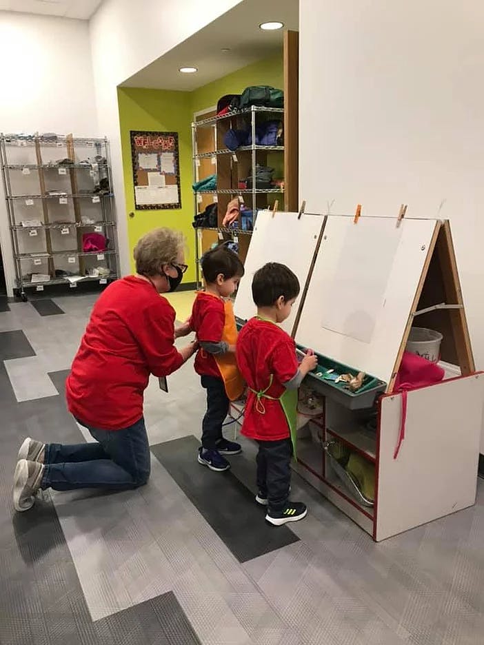 Person kneeling and two children painting at an easel