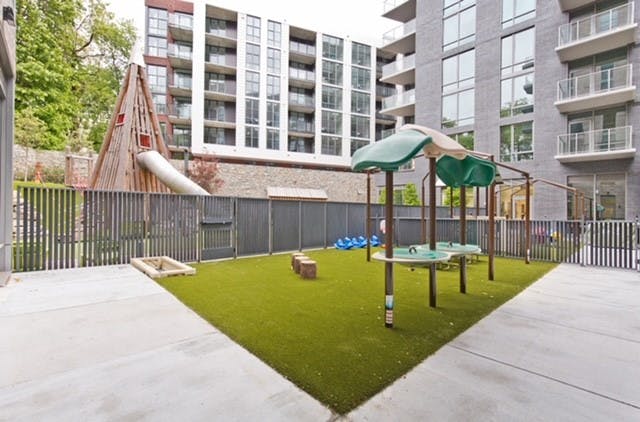 Playground with green turf, a wooden play structure, and other play equipment