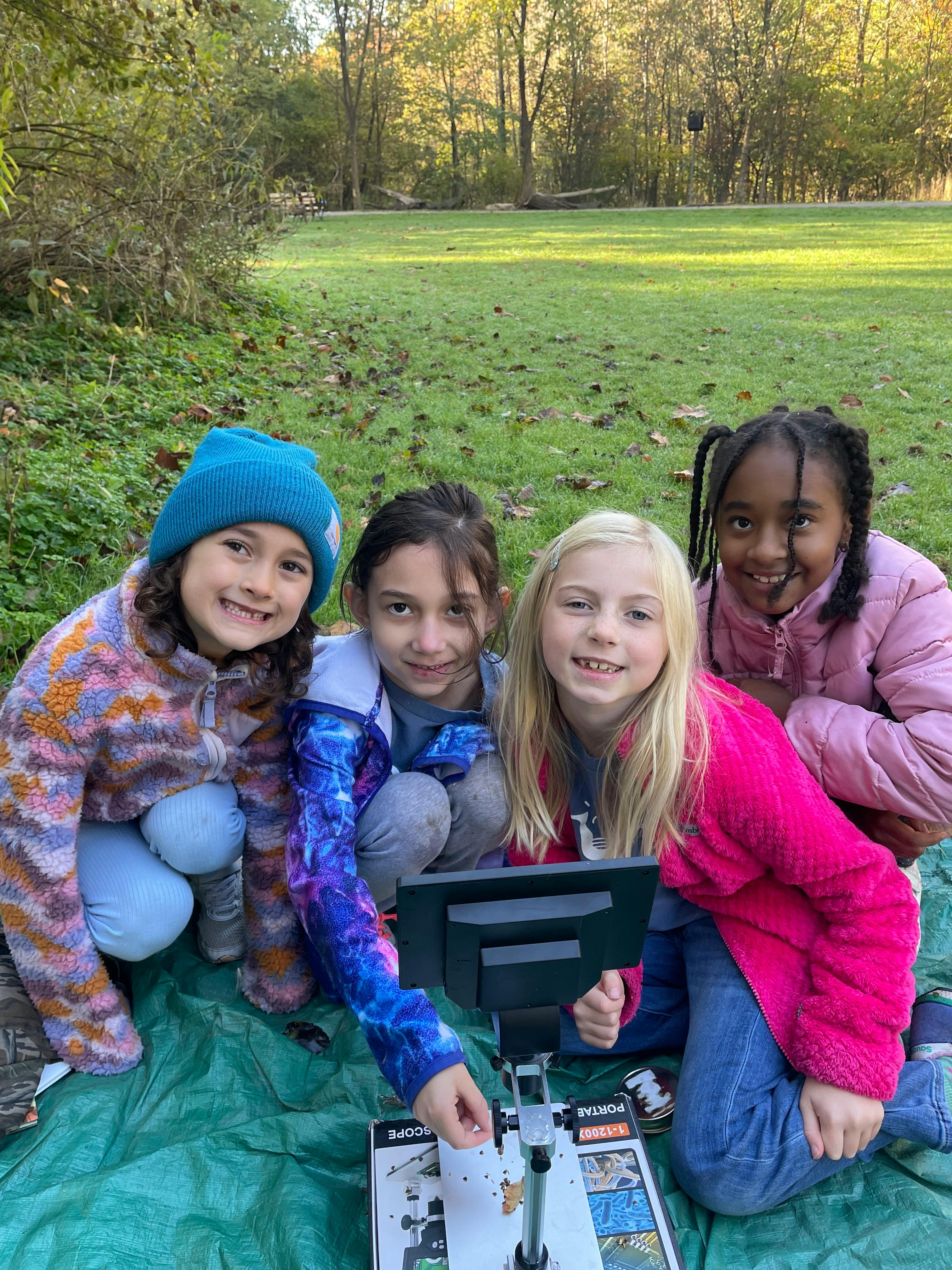 Four children kneeling around a microscope outdoors