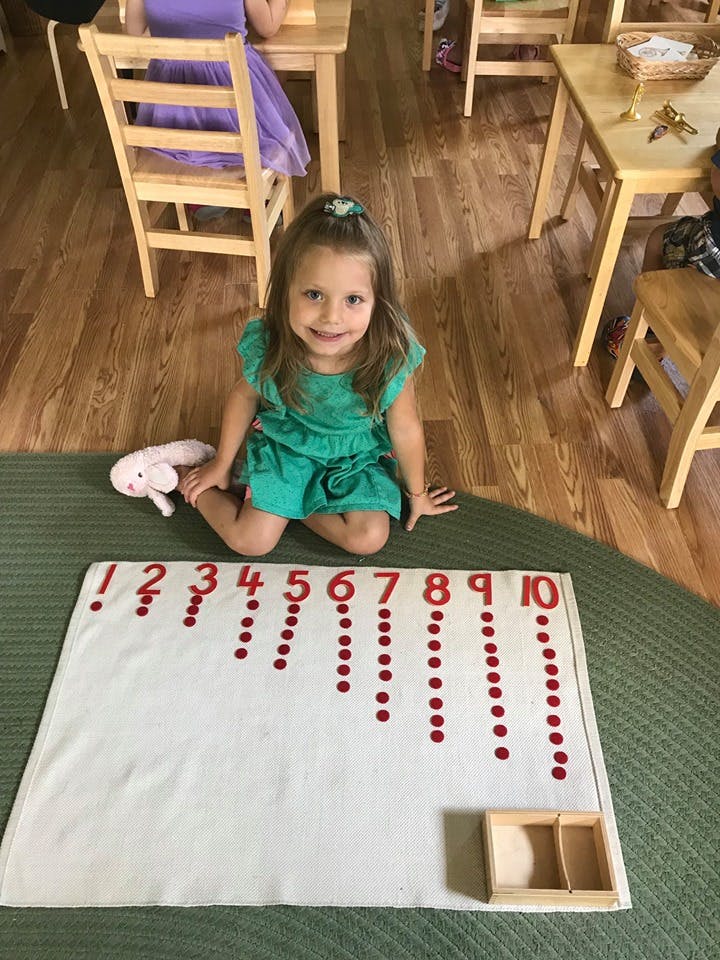 Child kneeling on floor next to a counting mat with numbers 1-10