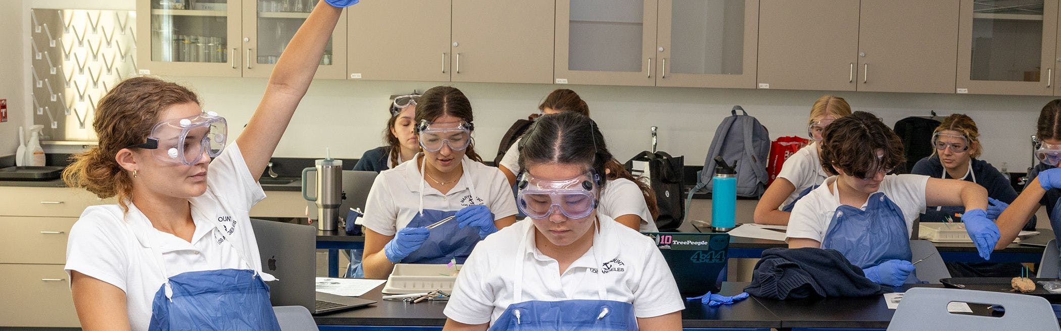 Students in safety goggles and aprons working on a lab project in a classroom