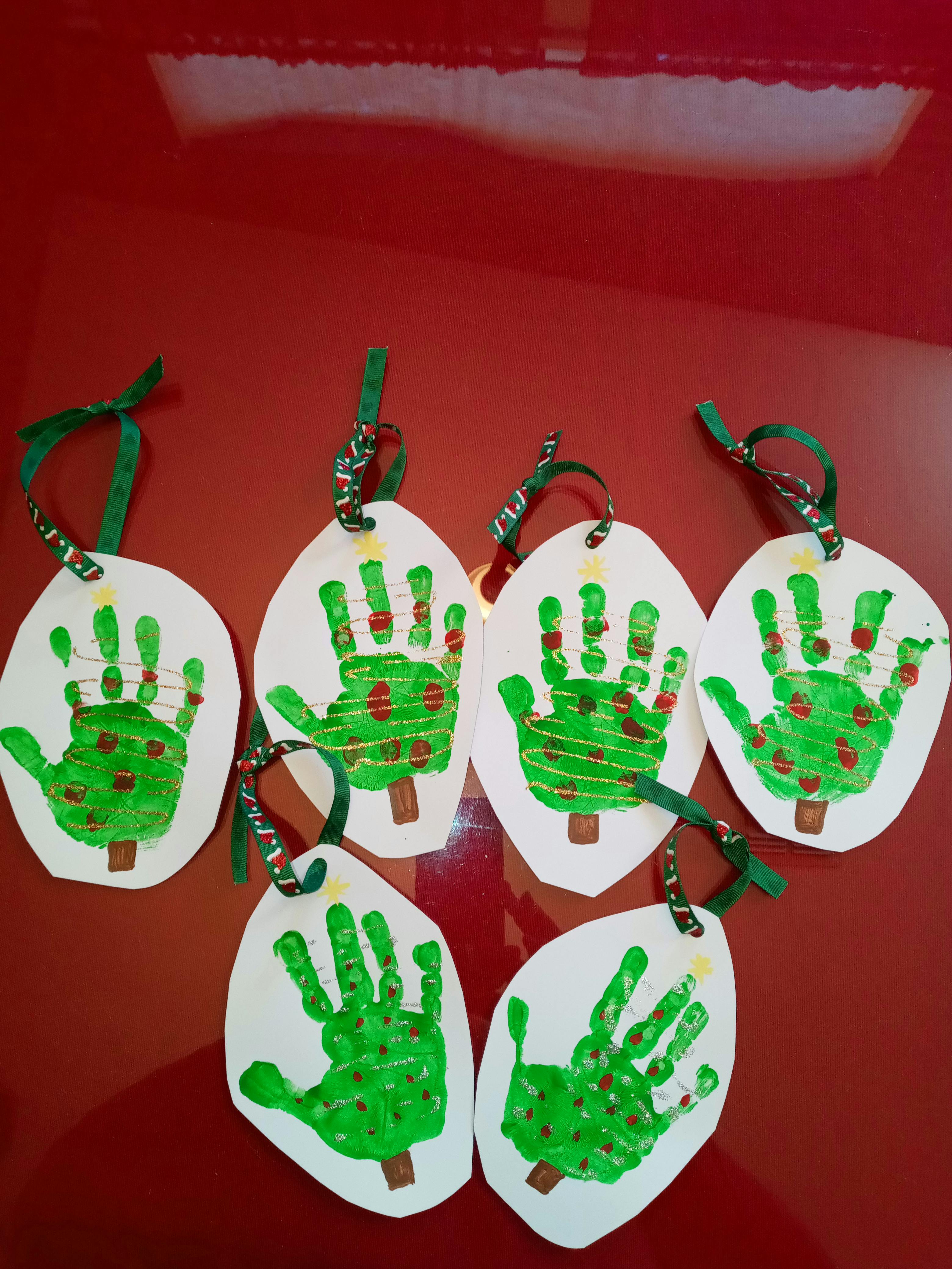 Multiple handprint Christmas tree ornaments with green ribbons