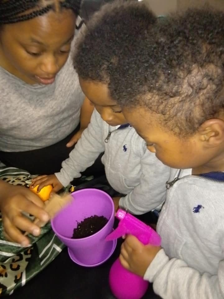 Person and two children looking at a purple pot with soil