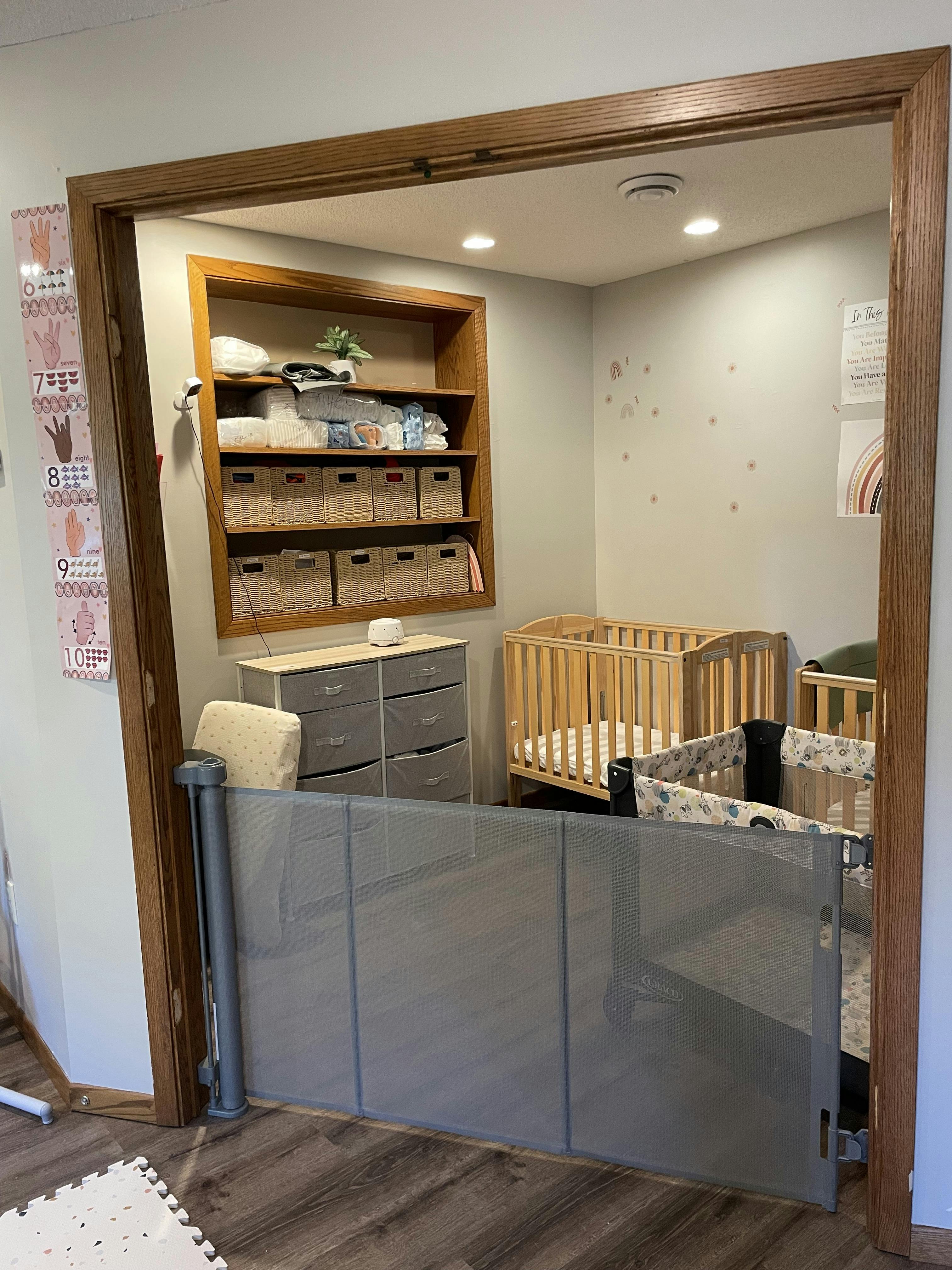 Nursery room with cribs, changing table, and storage shelves behind a baby gate