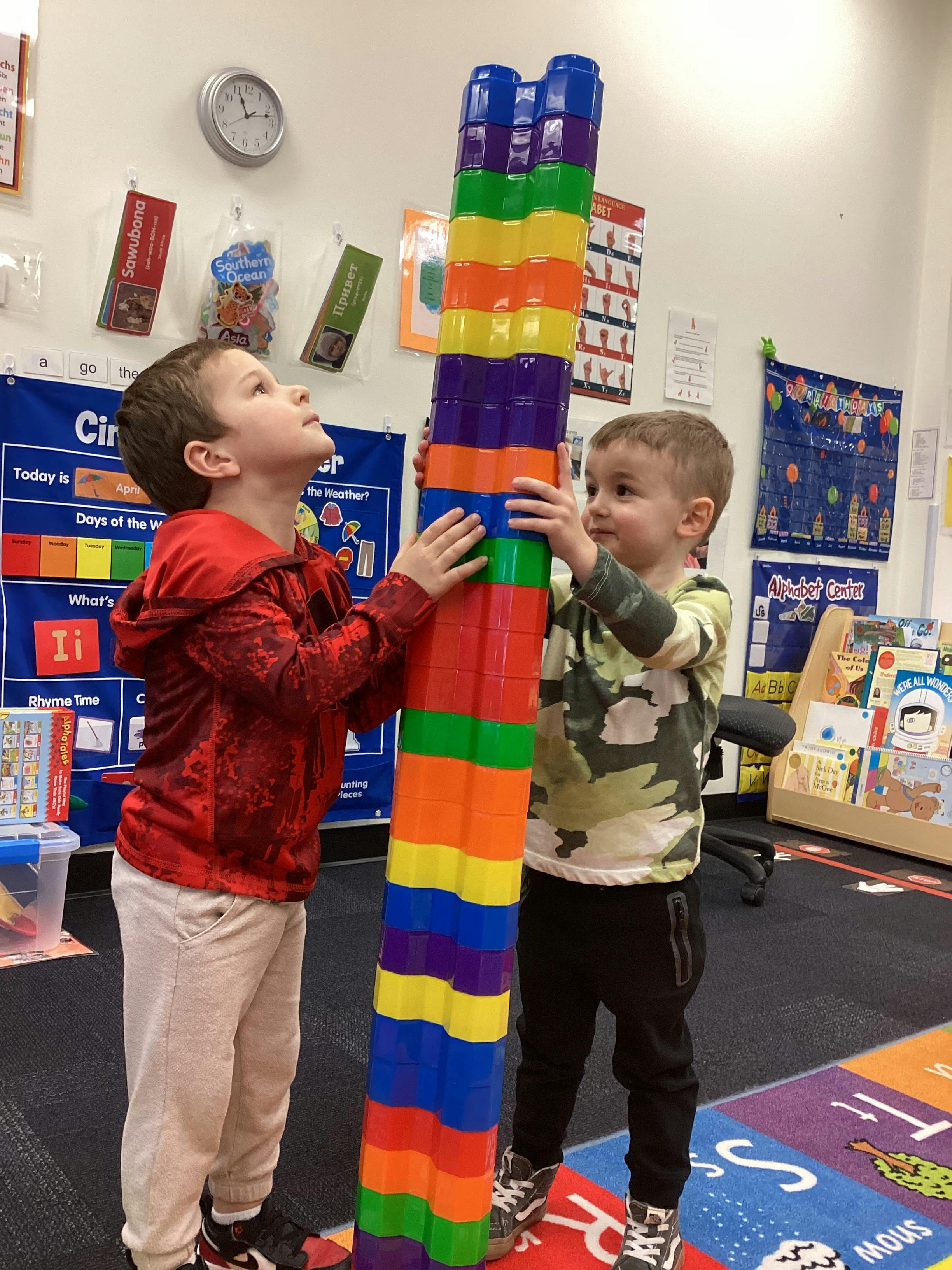 Two children building a tall tower of colorful plastic cups in a classroom