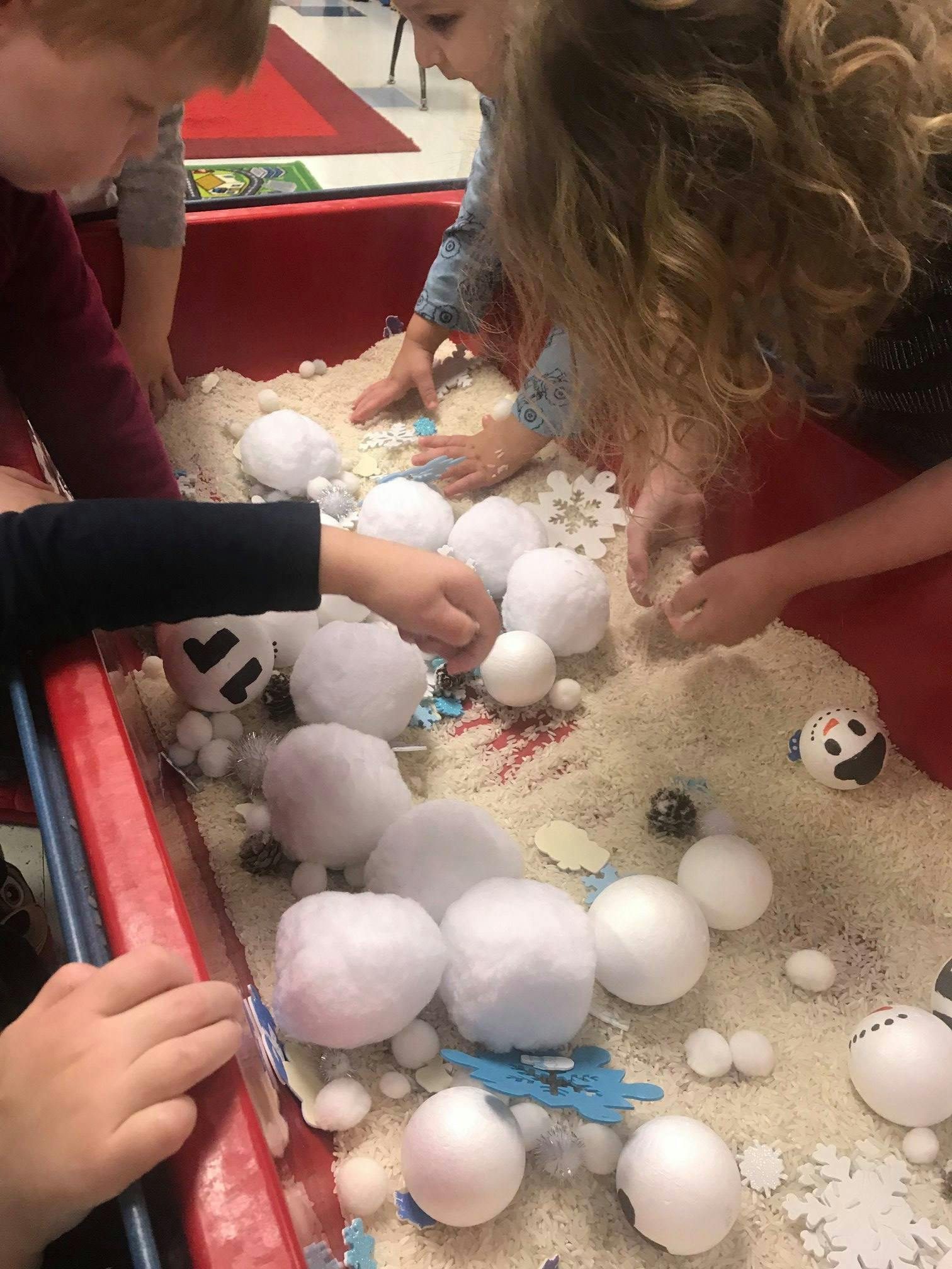 Children playing with white balls and snowflakes in a sensory bin